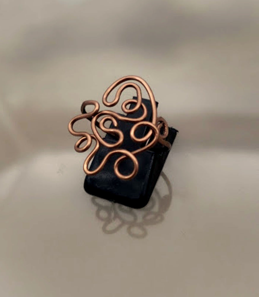 Handcrafted antiqued copper expression ring showing sculptural wire design on black base